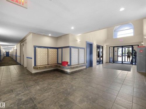 Spacious building lobby featuring tiled flooring, a bank of mailboxes with a stone-finish counter, and a vaulted ceiling with an arched transom window - #220 245 Edwards Dr Sw, Edmonton, AB - Indoor Photo Showing Other Room