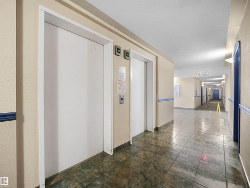 Two white elevator doors with call buttons, set against a cream-colored wall - #220 245 Edwards Dr Sw, Edmonton, AB - Indoor Photo Showing Other Room