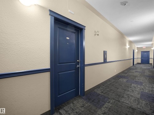 Hallway featuring textured walls, blue doors with molding, a patterned carpet, and wall-mounted light fixtures - #220 245 Edwards Dr Sw, Edmonton, AB - Indoor Photo Showing Other Room
