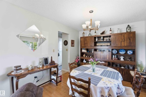 Charming dining and living space featuring hardwood flooring, a wood-finish built-in cabinet and shelving system with glass-front doors, a pendant light fixture, and a traditional dining table with ladder-back chairs - 30 Cavanagh Crescent, Stony Plain, AB - Indoor Photo Showing Dining Room