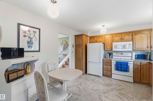 Wood-finish cabinetry paired with white appliances, tiled flooring, and a built-in pantry - 30 Cavanagh Crescent, Stony Plain, AB - Indoor Photo Showing Kitchen