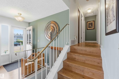 Wood-finish flooring throughout, a staircase with white balusters and a brass handrail, and a bright entryway with a paneled door - 30 Cavanagh Crescent, Stony Plain, AB - Indoor Photo Showing Other Room