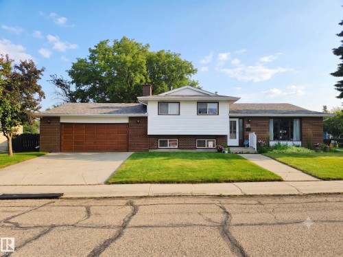 Traditional exterior featuring brick and white siding, an attached garage with a wood-finish door, a concrete driveway, and a front walkway - 30 Cavanagh Crescent, Stony Plain, AB - Outdoor With Facade