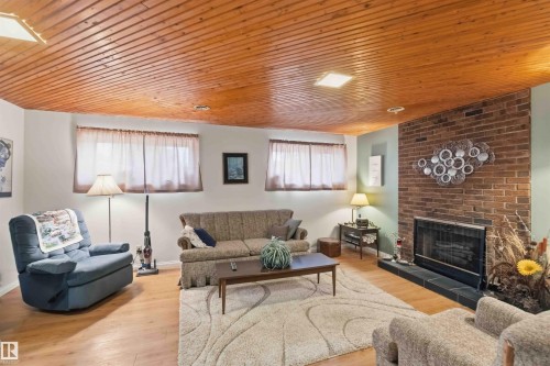 Wood-finish ceiling with integrated lighting, brick fireplace with a tile hearth, and wood-finish flooring - 30 Cavanagh Crescent, Stony Plain, AB - Indoor Photo Showing Living Room With Fireplace