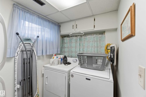 Dedicated laundry room featuring full-size front-load washer and dryer, white cabinetry with storage, sheer window treatments, and bright overhead lighting - 30 Cavanagh Crescent, Stony Plain, AB - Indoor Photo Showing Laundry Room