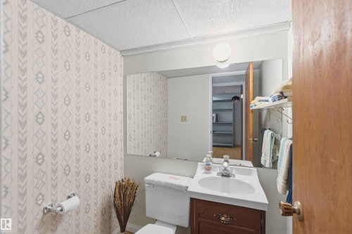 Vanity with integrated sink, wall-mounted mirror, and decorative wallpaper - 30 Cavanagh Crescent, Stony Plain, AB - Indoor Photo Showing Bathroom