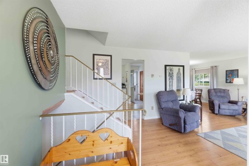 Wood-finish flooring throughout, white painted walls, and a staircase featuring white balusters with a brass-finish handrail - 30 Cavanagh Crescent, Stony Plain, AB - Indoor Photo Showing Other Room