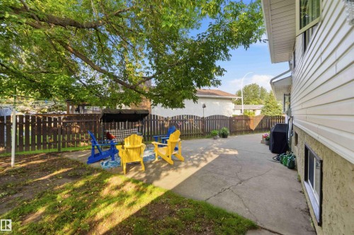 Spacious backyard retreat featuring a concrete patio, mature shade trees, wooden privacy fencing, and colorful Adirondack seating areas - 30 Cavanagh Crescent, Stony Plain, AB - Outdoor With Exterior
