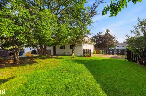 Expansive backyard featuring a manicured lawn, mature trees providing natural shade, and a wood picket fence - 30 Cavanagh Crescent, Stony Plain, AB - Outdoor