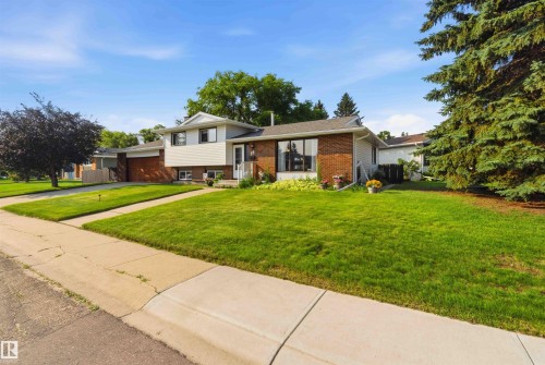 Split-level residence featuring a brick and white siding facade, attached garage, concrete driveway, and a front lawn with mature trees - 30 Cavanagh Crescent, Stony Plain, AB - Outdoor