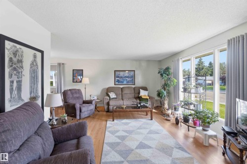 Wood-finish flooring, light-toned wall paint, large windows with neutral drapes, and a textured ceiling - 30 Cavanagh Crescent, Stony Plain, AB - Indoor Photo Showing Living Room