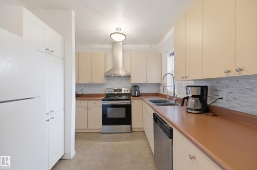 Kitchen featuring light-toned cabinetry, stainless steel appliances, a mosaic tile backsplash, and a double basin sink with a gooseneck faucet - 10714 103 Street Nw, Edmonton, AB - Indoor Photo Showing Kitchen With Double Sink