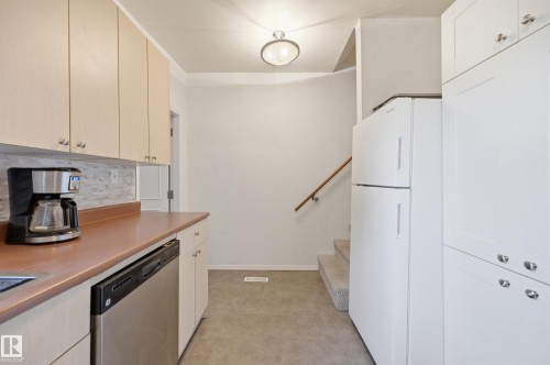 Kitchen area featuring light wood-finish upper cabinetry, a stainless steel dishwasher, a white refrigerator, a tile backsplash, and durable flooring - 10714 103 Street Nw, Edmonton, AB - Indoor Photo Showing Kitchen