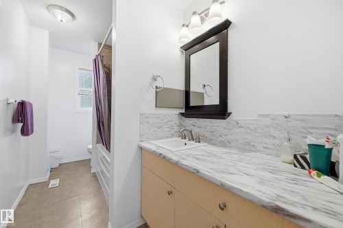 Bathroom vanity featuring a light wood-finish cabinet with silver hardware, a white countertop with grey veining, and a complementary white tile backsplash - 10714 103 Street Nw, Edmonton, AB - Indoor Photo Showing Bathroom
