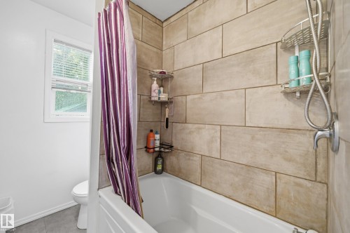 Bathtub and shower combination featuring light-toned rectangular wall tiling, a white bathtub, and a window with blinds - 10714 103 Street Nw, Edmonton, AB - Indoor Photo Showing Bathroom