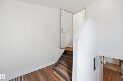 Staircase with wood-finish treads and risers, complemented by a solid white wall and a panel door leading to an upper level - 10714 103 Street Nw, Edmonton, AB - Indoor Photo Showing Other Room
