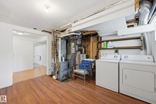 Laundry area featuring wood-finish flooring, washer and dryer appliances, and wall-mounted shelving - 10714 103 Street Nw, Edmonton, AB - Indoor Photo Showing Laundry Room