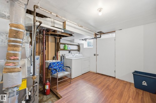 Laundry area featuring wood-finish flooring, a utility sink, and white walls - 10714 103 Street Nw, Edmonton, AB - Indoor Photo Showing Laundry Room