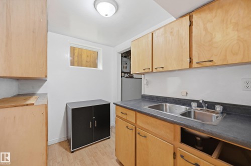 Utility space featuring wood-finish flooring, light wood cabinetry, a dual basin stainless steel sink, and a high window - 10714 103 Street Nw, Edmonton, AB - Indoor Photo Showing Kitchen With Double Sink