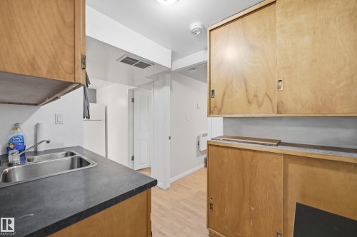 Kitchenette featuring wood-finish cabinetry, a double basin stainless steel sink, and dark countertops - 10714 103 Street Nw, Edmonton, AB - Indoor Photo Showing Kitchen With Double Sink