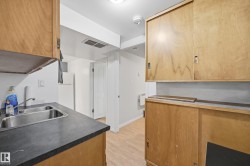 Kitchenette featuring wood-finish cabinetry, a double basin stainless steel sink, and dark countertops - 