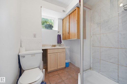 Three-piece bathroom featuring a ceramic tile shower enclosure with a clear glass door, a single vanity with wood-finish cabinetry, and a window - 10714 103 Street Nw, Edmonton, AB - Indoor Photo Showing Bathroom