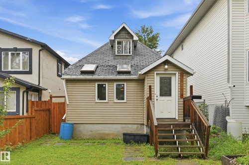 Rear exterior featuring tan horizontal siding, a gabled entry with wooden stairs, a shingled roof with multiple skylights, and a dormer window - 10714 103 Street Nw, Edmonton, AB - Outdoor