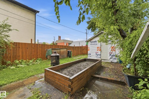 Enclosed backyard featuring a wood fence, mature trees, a raised garden bed, and a shed structure - 10714 103 Street Nw, Edmonton, AB - Outdoor