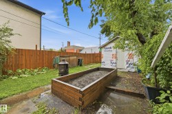Enclosed backyard featuring a wood fence, mature trees, a raised garden bed, and a shed structure - 