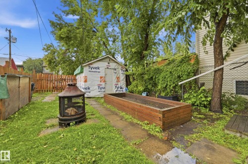 Expansive backyard featuring a partially-wrapped storage shed, a wood-finish raised garden bed, a metal fire pit, and mature trees - 10714 103 Street Nw, Edmonton, AB - Outdoor