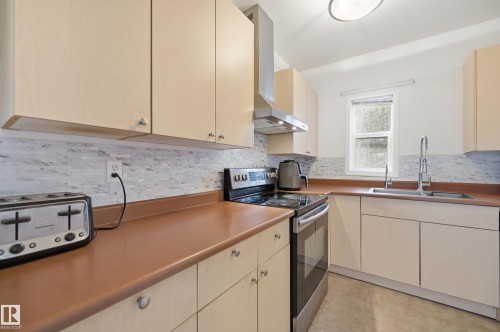 Kitchen featuring light wood-finish cabinetry, a mosaic tile backsplash, stainless steel appliances, and a single window - 10714 103 Street Nw, Edmonton, AB - Indoor Photo Showing Kitchen With Double Sink