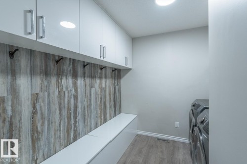 Laundry area with white cabinetry, wood-finish flooring, a built-in bench, and a panel wall with hooks - 1724 27 Street Nw, Edmonton, AB - Indoor