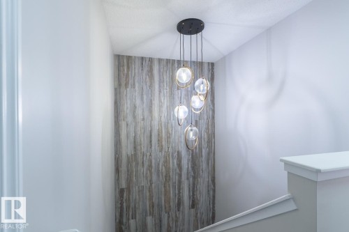 Multi-globe chandelier with gold-tone accents and a black ceiling mount, illuminating a vertical wood-finish accent wall - 1724 27 Street Nw, Edmonton, AB - Indoor