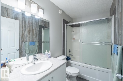 Full bathroom featuring a white vanity with an undermount sink, a large mirror, a chrome light fixture, a toilet, and a combination tub and shower with a frosted glass enclosure - 1724 27 Street Nw, Edmonton, AB - Indoor Photo Showing Bathroom