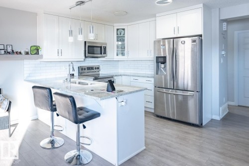 Open-concept kitchen featuring white shaker cabinetry, stainless steel appliances, a subway tile backsplash, and light-toned countertop surfaces - 1724 27 Street Nw, Edmonton, AB - Indoor Photo Showing Kitchen