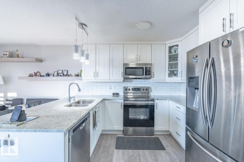 Modern kitchen featuring light wood-finish flooring, white cabinetry, stainless steel appliances, and a subway tile backsplash - 1724 27 Street Nw, Edmonton, AB - Indoor Photo Showing Kitchen With Double Sink With Upgraded Kitchen