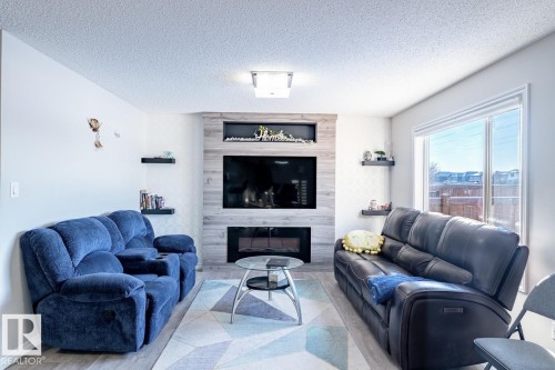 Living area featuring a floor-to-ceiling accent wall with a built-in fireplace, integrated shelving, and wood-finish paneling - 1724 27 Street Nw, Edmonton, AB - Indoor Photo Showing Living Room With Fireplace