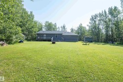 Expansive green lawn extending to a treed perimeter, featuring a rear exterior with a deck, a separate storage shed, and mature trees providing natural screening - 