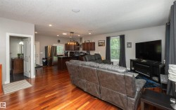 Open-concept living area with wood-finish flooring, recessed lighting, and a kitchen featuring dark wood cabinetry, stainless steel appliances, and an island with pendant lighting - 