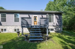 Exterior showcasing a wooden entry deck with dark railings, a wood-paneled door with an oval glass insert, and a foundation accented with stone veneer - 