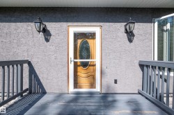 Entryway featuring a wood-panel door with oval glass insert, white storm door, and textured gray stucco exterior - 
