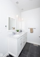 Dual white vanity with undermount sinks and a light-toned countertop, featuring chrome fixtures and two framed mirrors - 