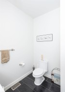 White-walled powder room featuring a white toilet, dark rectangular tile flooring, and white baseboards - 