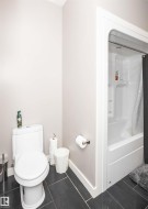 Bathroom featuring a white toilet, contemporary black tile flooring, and a shower-over-tub combination with a white surround - 