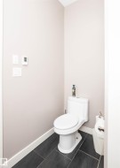 Bathroom featuring a white toilet, dark large-format floor tiles, and light-toned walls - 
