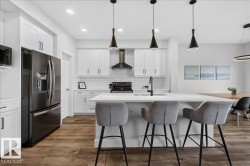 Modern kitchen featuring a large center island with integrated sink, white shaker-style cabinetry, a white subway tile backsplash, and wood-finish flooring - 