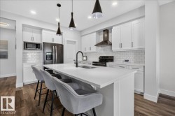 Bright kitchen featuring a substantial island with integrated sink, white cabinetry with dark hardware, subway tile backsplash, stainless steel appliances, and wood-finish flooring - 