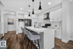 Modern kitchen featuring a large island with seating, white cabinetry, dark hardware, subway tile backsplash, and wood-finish flooring - 