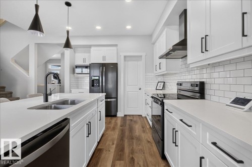 Modern kitchen featuring white shaker cabinetry, stainless steel appliances, a subway tile backsplash, and wood-finish flooring - 3805 Cherry Loop Sw, Edmonton, AB - Indoor Photo Showing Kitchen With Double Sink With Upgraded Kitchen