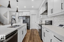 Modern kitchen featuring white shaker cabinetry, stainless steel appliances, a subway tile backsplash, and wood-finish flooring - 